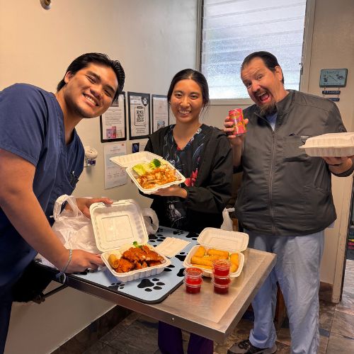 Three people smiling and posing for a photo while holding various dishes of food.